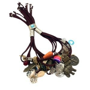 Pulsera de Gamuza con dijes de diferentes metales, flecos, muñequitas y flores vino